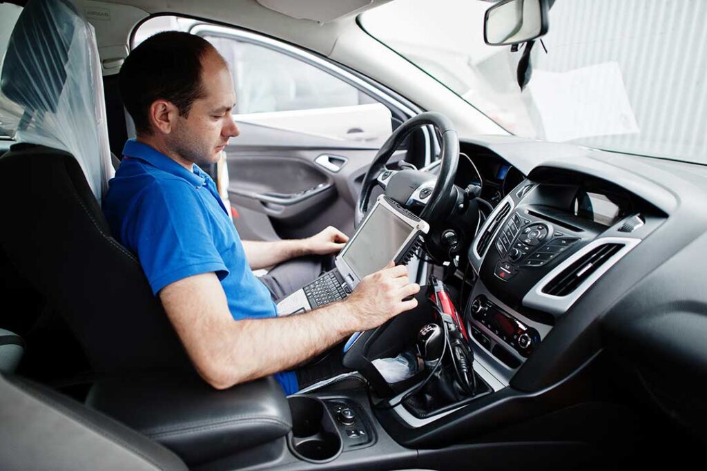 A person holding car keys and a clipboard while inspecting a used car’s dashboard and VIN.