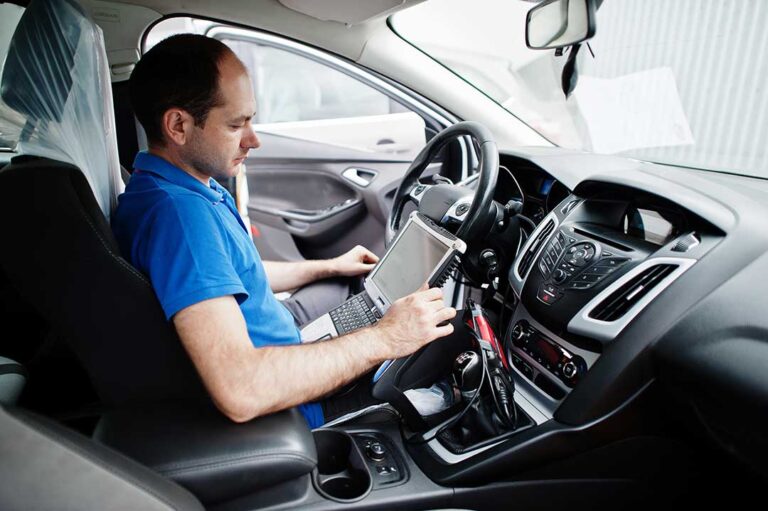 A person holding car keys and a clipboard while inspecting a used car’s dashboard and VIN.