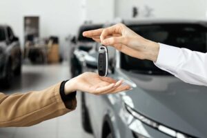 A buyer examines a vehicle window sticker through the side glass while comparing listed features and prices.